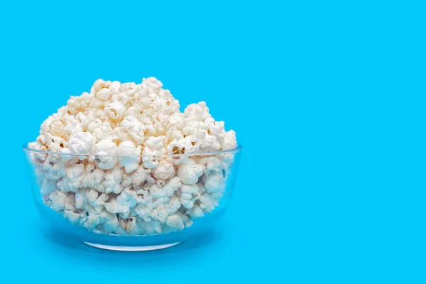 Popcorn in a large glass bowl on a blue background. Crispy classic popcorn snack for watching movies and series. Delicious snack for spending free time and watching TV