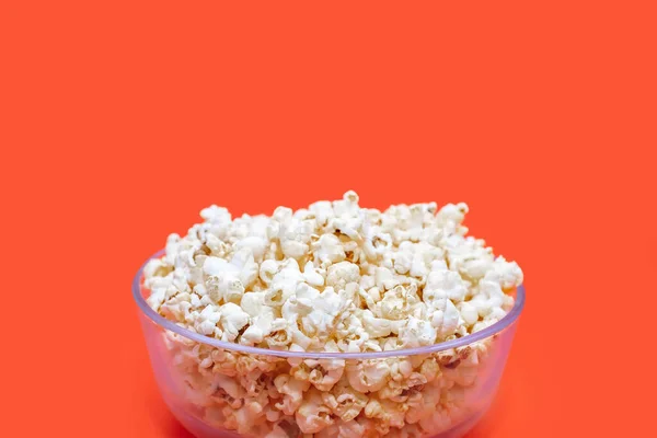 Popcorn in a large glass bowl on an orange background close-up. Crispy classic popcorn snack for watching movies and TV series. Delicious snack for spending free time and watching TV