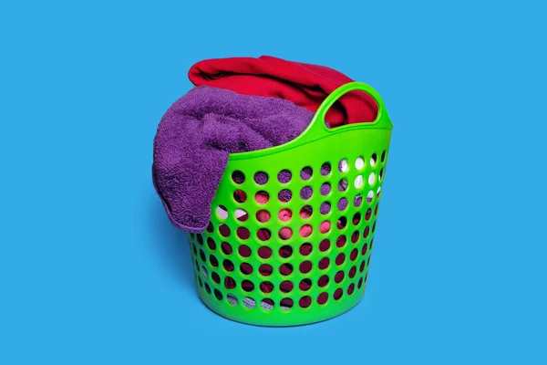 Dirty clothes in a plastic green laundry basket on a blue background. Housekeeping and laundry concept. Dirty clothes are placed in the basket and are ready to be washed