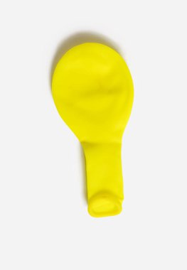 Yellow balloon deflated on a white isolated background. One uninflated balloon from above. The concept of preparing for the holiday in the form of decoration with balloons