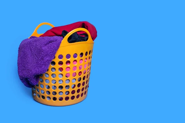 Dirty clothes are folded into a plastic orange laundry basket on a blue background. Housekeeping and laundry concept. Dirty clothes lie in the basket and are ready for washing. Free space for text