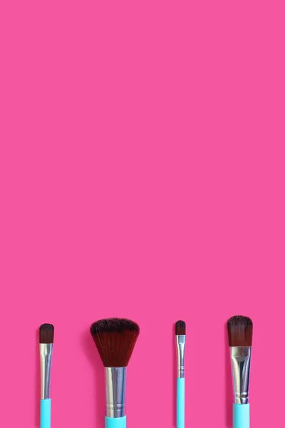 A set of four makeup brushes on a pink vertical background. Four blue makeup brushes in different shapes and sizes. Fashionable women\'s cosmetics to create facial beauty. Free space for text