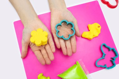 Çocuk yumuşak plastikinle oynuyor ve pembe bir tahtaya farklı şekiller çiziyor. Çocuğun elleri, çiçek şeklinde sarı bir plastikini tutar. Çocuğun yaratıcı gelişimi