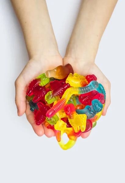 stock image A large pile of multi-colored jelly marmalade candies in the hands of a child on a white background. Variety of tasty bright chewing gums. Various delicious gummy candies in hands close-up top view