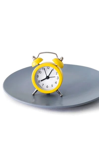 一个黄色的闹钟矗立在一个白色垂直背景的盘子上 饮食和适当营养的概念在时间表上 午餐休息时间或就餐时间 严格按照约定的时间吃饭 — 图库照片