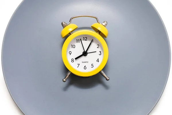 一只黄色的闹钟停在白色背景的盘子上 饮食和适当营养的概念在时间表上 午餐休息时间或就餐时间 严格按照约定的时间吃饭 — 图库照片