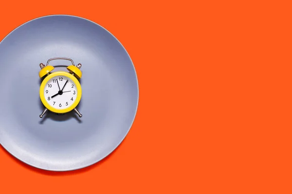 橙色背景的盘子上躺着一只黄色的闹钟 节食和按时吃饭的概念 亮黄色闹钟和灰色盘子 文字和广告的自由空间 — 图库照片