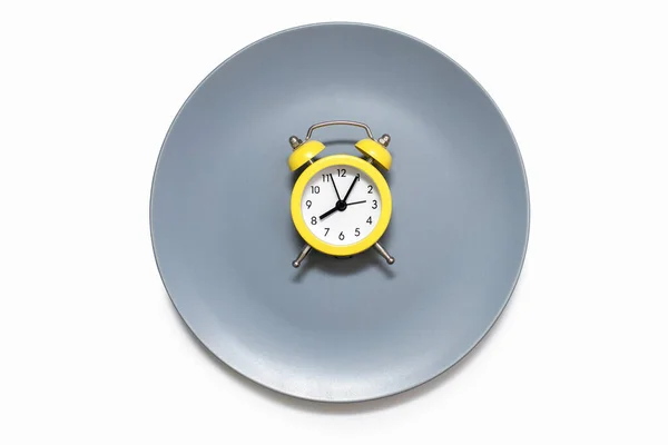 一只黄色的闹钟停在白色背景的盘子上 按时饮食和适当营养的概念 亮黄色闹钟和灰色盘子 — 图库照片