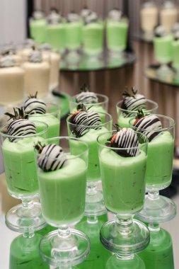 Kivi aromalı yoğurt kreması ve tepside cam bardaklarda çikolata kaplı çilek. Lezzetli tatlı. Kivi aromalı panna cotta. Restoranda sağlıklı meyve tatlısı.