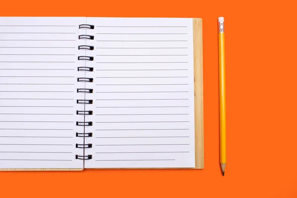 An open notebook with a binding and a yellow pencil on an orange background. Open notepad with blank sheets in top view. Free space for text. Blank notebook pages ready to be used in design