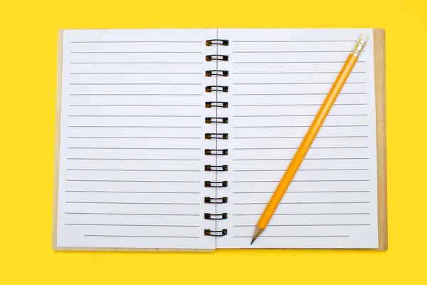 An open notebook with a binding and a pencil on a yellow background. Open notepad with blank sheets in top view. Free space for text. Blank notebook pages ready to be used in design