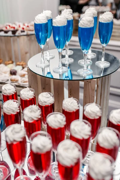 Red and blue fruit jelly with air cream on top in glass goblets on a tray. Delicious dessert for a big company in a restaurant. Jelly dessert beautifully decorated with cream in glasses