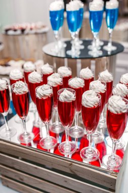 Tepside cam kadehler içinde beyaz kremalı kırmızı ve mavi jöle. Restorandaki büyük bir şirket için lezzetli bir tatlı. Gözlüklü kremayla süslenmiş jöleli tatlı.