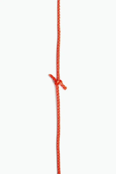 赤いロープの両端は 白い縦の背景に結び目で結ばれています 中央に結び目を持つ赤いナイロンロープ テキストと広告のためのフリースペース — ストック写真