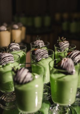 Kivi aromalı yoğurt kreması ve tepside cam bardaklarda çikolata kaplı çilek. Lezzetli tatlı. Kivi aromalı panna cotta. Çilekli bir restoranda meyveli tatlı.