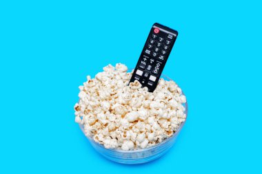 Cam kasede patlamış mısır ve mavi arka planda uzaktan kumanda. Film ya da dizi izleyerek ve patlamış mısır yiyerek boş zaman kavramı. Patlamış mısır ve televizyon uzaktan kumandası görüntüsü