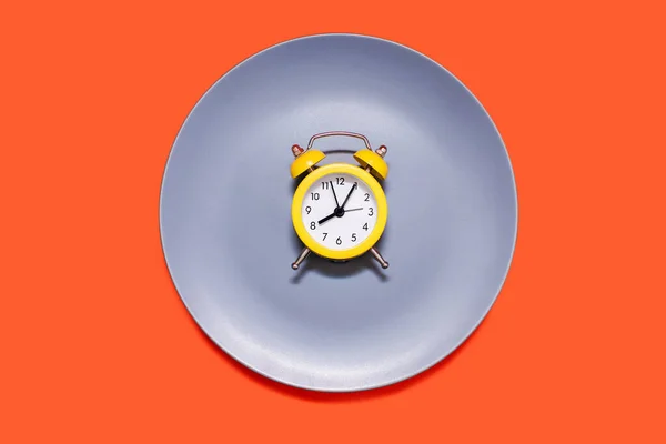 橙色背景的盘子上躺着一只黄色的闹钟 节食和按时吃饭的概念 亮黄色闹钟和灰色盘子 — 图库照片