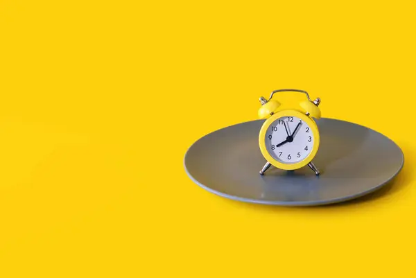 闹钟在一个黄色背景的盘子上 饮食和适当营养的概念在时间表上 黄色的闹钟和灰色的盘子文字和广告的自由空间 — 图库照片