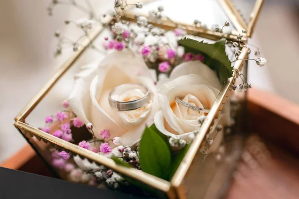 新娘和新郎的结婚戒指装在一个用白玫瑰装饰的玻璃盒里 婚礼上的结婚戒指 漂亮的新娘和新郎戴着白金戒指 — 图库照片