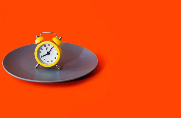 警钟在橙色背景的盘子上 饮食和适当营养的概念在时间表上 黄色的闹钟和灰色的盘子文字和广告的自由空间 — 图库照片