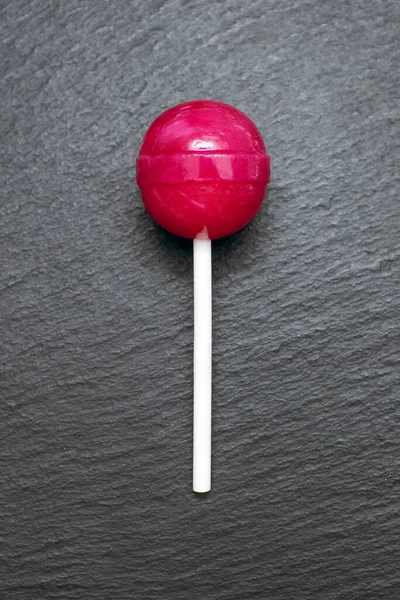 赤いロリポップが荒々しい黒の背景にあります スティック上の古典的な甘いキャンディー 子供のための甘いデザートコンセプト — ストック写真
