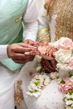 Damat, Hint düğün töreninde gelinin parmağına elmas bir yüzük takar. Gelinin ellerinde geleneksel Hint desenleri şeklinde kınalar çiziyor.