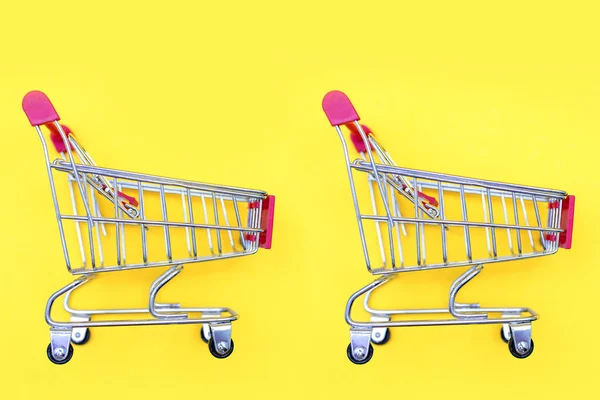 Two toy shopping carts in a supermarket on a yellow background. The concept of trade and shopping. Wholesale and retail trade. Free place for text or design idea