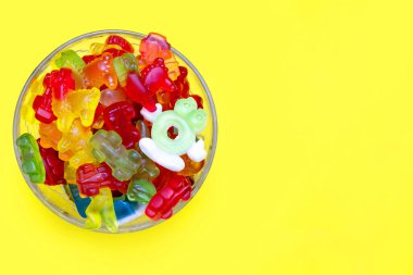 Sarı arka planda cam bir kasede çok renkli jelibon şekerler yığını. Lezzetli sakızların çeşitleri. Cam bir kapta çeşitli lezzetli yapışkan şekerler var. Metin için boş alan