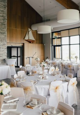 Düğün ve resepsiyonlar için ayrılmış masaları olan büyük bir restoran. Misafirlerin resepsiyonu için restoranın hazırlıkları. Dikey bir resimde çiçeklerle süslenmiş tablolar