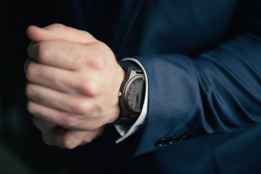 Mavi takım elbiseli bir adam ve klasik bir tahta mekanik saat. Ekolojik ahşap saati olan yakın plan bir adam. Tahtadan yapılmış mekanik kol saati. Bir adam toplantıya gidiyor ve bir saat takıyor.