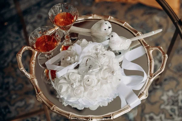 婚戒放在白色枕头上 两杯白兰地放在盘子里 以金戒指和酒精为形式的婚礼饰物 新郎新娘结婚纪念日和结婚戒指 — 图库照片