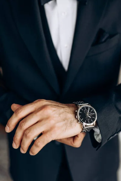 The man is dressed in a classic suit and an expensive wrist watch. Close-up of a mechanical watch on a man\'s hand. The concept of punctuality and confidence. A man puts on his wristwatch