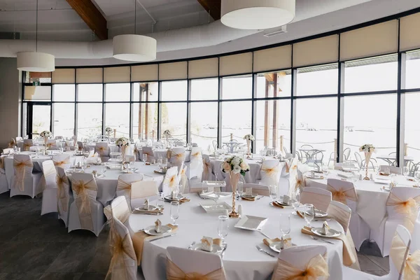 Large restaurant with huge windows with reserved tables for a wedding party. Preparation of the restaurant for the reception of guests. The tables in the restaurant are decorated with flowers