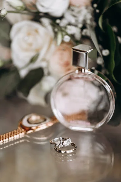 Wedding accessories of the bride in the form of a bouquet of roses, wedding rings with precious stones and perfume. Bridal bouquet of white roses. Wedding rings with precious stones and watches