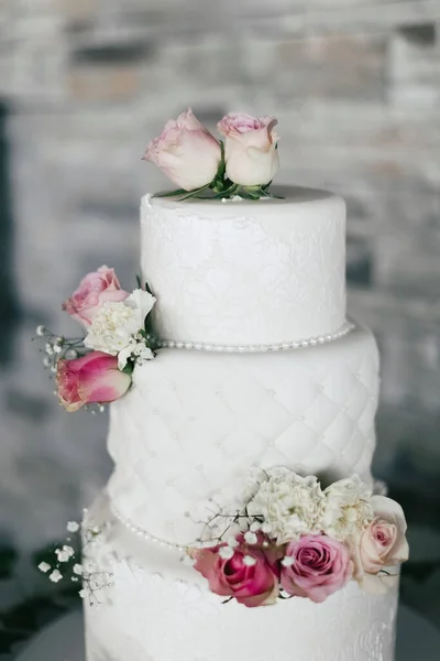 Gorgeous white wedding cake decorated with red roses. Luxurious multi-level cake in the restaurant for the bride and groom. Traditional cake at a wedding on a vertical close-up image