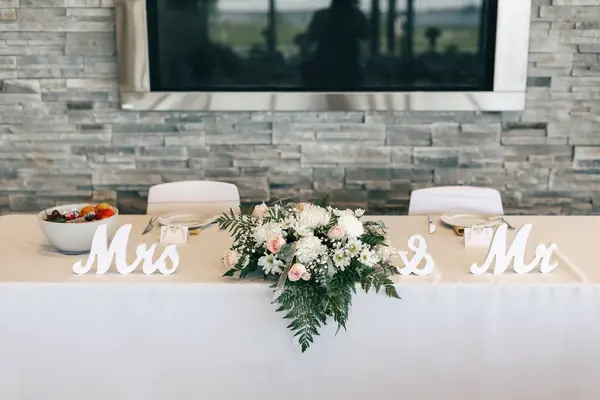 The table of the bride and groom in the restaurant is decorated with flowers and signs with the inscription Mr. and Mrs. Beautiful newlyweds table with white tablecloth and flowers