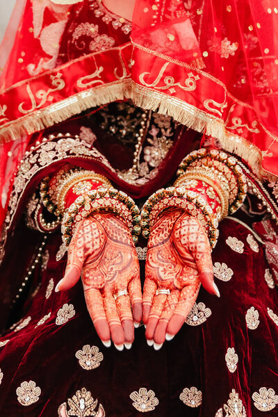 The hands of the Indian bride are decorated with curly red patterns in the form of traditional ornaments and bracelets. Beautiful drawings in the Indian style of henna on the palms of the bride