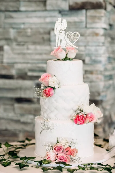 White wedding cake decorated with red roses and figurine in the shape of a bride and groom. Luxurious multi-level cake in the restaurant for the bride and groom. Traditional wedding cake