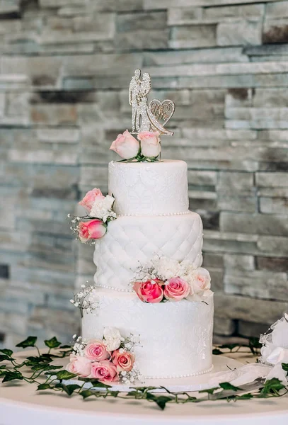 White wedding cake decorated with red roses and figurine in the shape of a bride and groom. Luxurious multi-level cake in the restaurant for the bride and groom. Traditional wedding cake with flowers