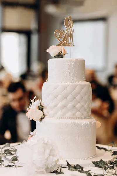 White wedding cake decorated with patterns and a figurine in the form of a bride and groom. Luxurious tiered cake in a restaurant for a wedding party. Traditional wedding cake decorated with flowers