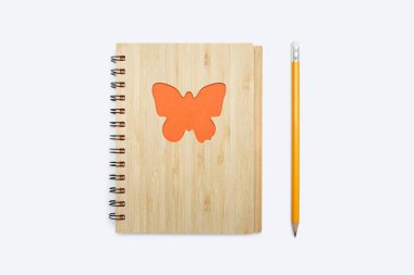 Kapalı defter, üzerinde turuncu bir kelebek süsü ve sarı bir kalem olan bir babmouk kapağı var. Not defteri ve beyaz arkaplanda bir kalem şeklinde kırtasiye malzemesi