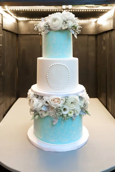 Tiered wedding cake decorated with roses and white flowers. Beautiful wedding cake for the bride and groom and their guests. Chic and delicious confectionery in the form of a cake for a wedding party