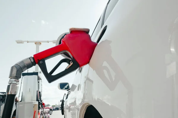 Refueling a white car with fuel at a gas station. The car fills up with gasoline at a gas station. Gas station pump. Fuel is poured into the car using a nozzle. Red handle for refueling auto fuel
