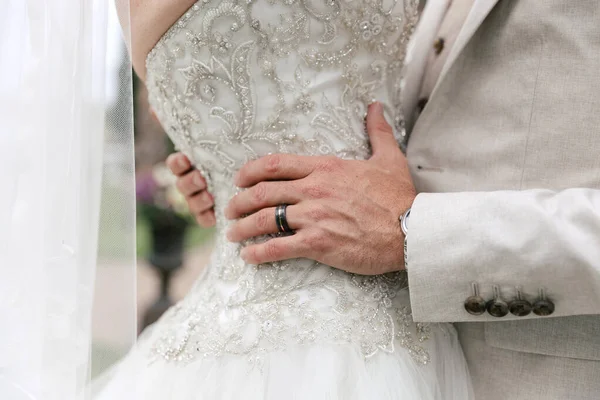 The groom hugs the bride by the waist during the wedding ceremony. Hugs of the bride and groom close-up. Wedding ring on the groom\'s finger. Beautiful wedding dresses for the bride and groom