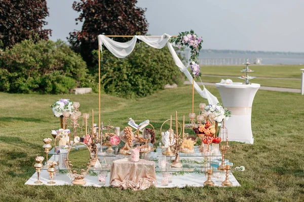 The arch for the wedding ceremony stands on the lawn and is decorated with flowers. Beautiful decoration of the wedding ceremony consisting of candles and treats. Preparing for the wedding