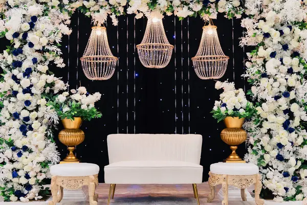 A beautiful decorated place for the wedding ceremony of the bride and groom in oriental style. Wedding arch made of white and blue fresh flowers. Beautiful decorative chandeliers and a white bench