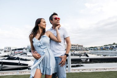 Şık bir adam ve güzel bir kadın limandaki yatların arka planında poz veriyorlar. Birbirine aşık bir çift, bir erkek ve bir kadın, boş zamanlarını dışarıda geçirirler.