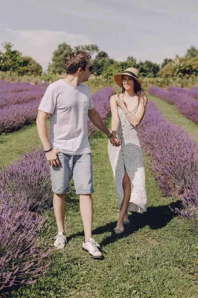 A couple in love walks through a lavender field. A woman in a dress and a straw hat with a man hold hands and walk through a purple lavender field. Romantic relationship. Unity with nature