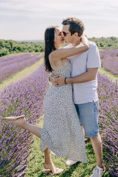 A couple in love hugs and kisses in a purple lavender field. Romantic relationship between a young woman and a man. Lovers hug and kiss. Heterosexual couple. Lovers walk through a flowering meadow