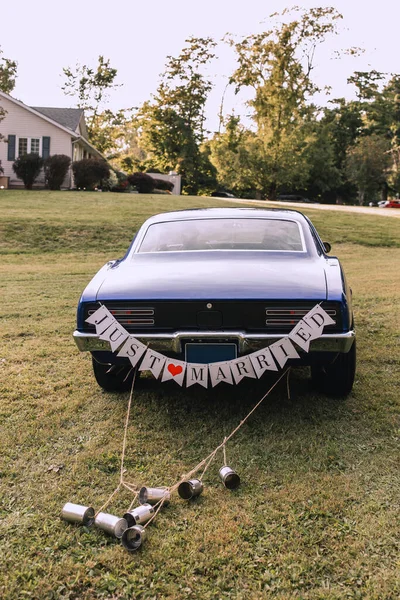 The wedding car with just married sign and cans tied to the trunk. The car for the newlyweds is parked in the backyard. Dark blue car for brides. Wedding day